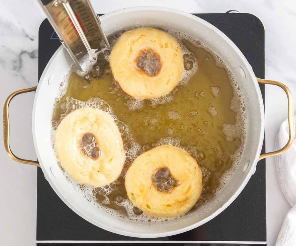Three French cruller doughnuts frying in a pan.