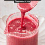 Blackberry icing being poured into a small glass jug.