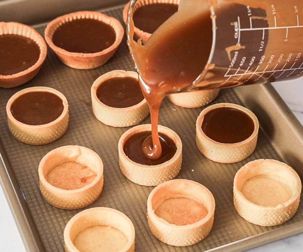 Butterscotch being poured from a jug into the tartlet shells.