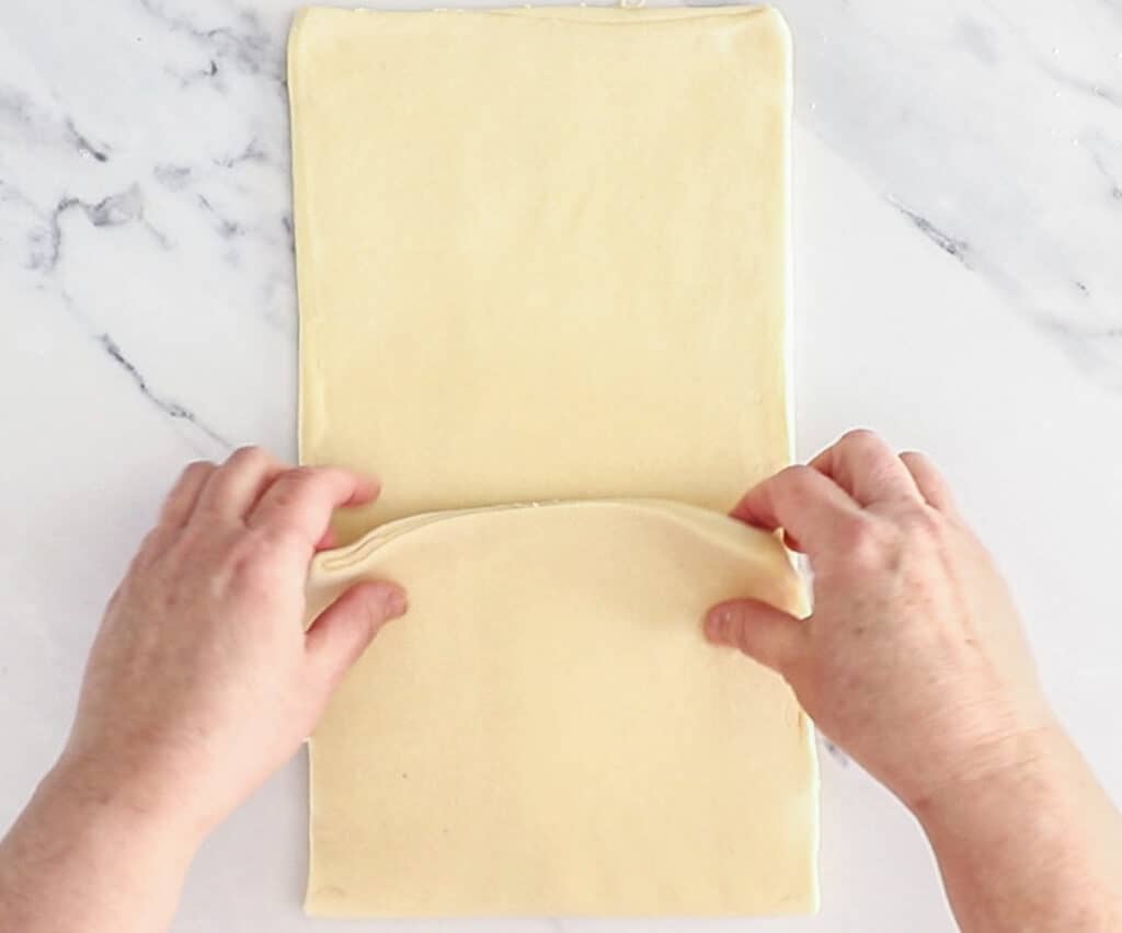 Hands folding the pain au chocolat dough into the centre.