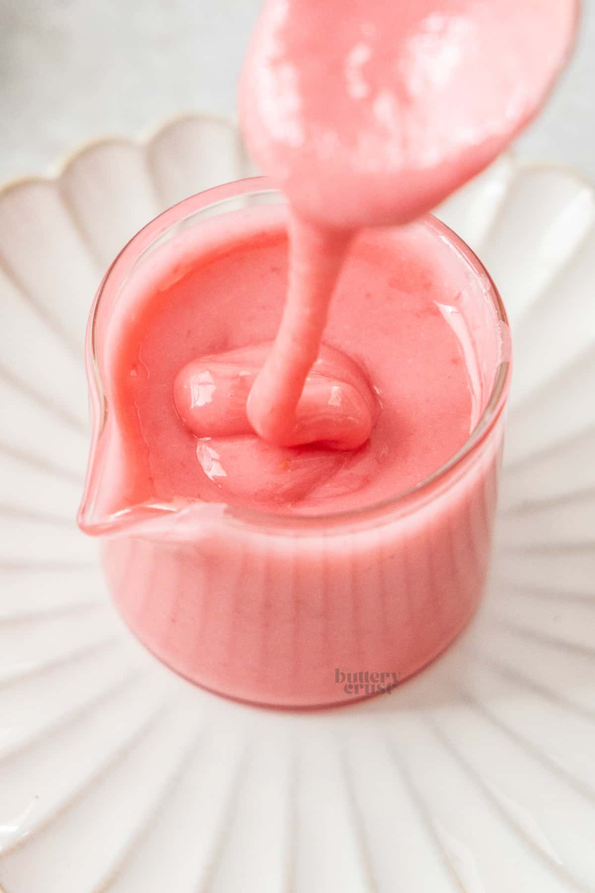 Raspberry icing being drizzled into a glass jar.