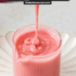Raspberry icing being drizzled into a glass jar.