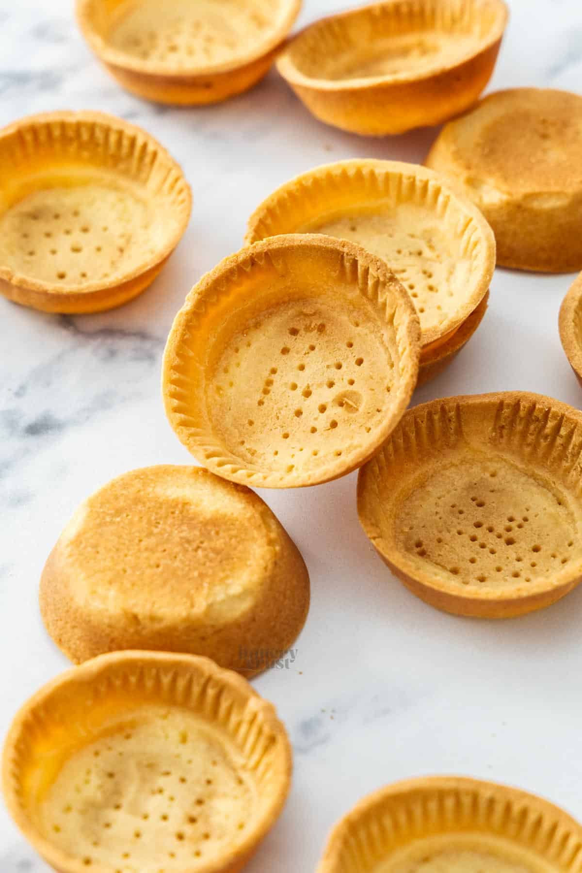 A pile of tartlet shells made in a muffin pan.