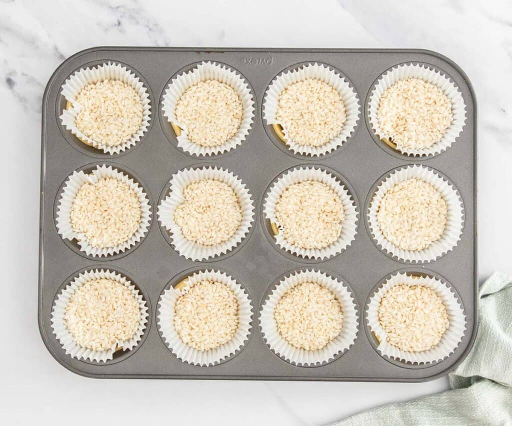 The raw tart shells in a muffin pan with cupcake papers and rice in each one.