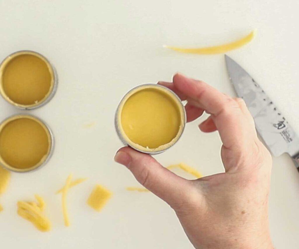 A hand holding a mini tart shell in a tart ring up to the camera.