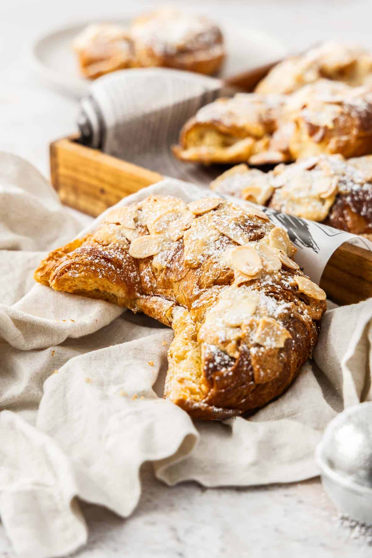 An almond croissant next to a wooden serving tray.