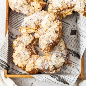 Top down view of five almond croissants on a wooden tray.