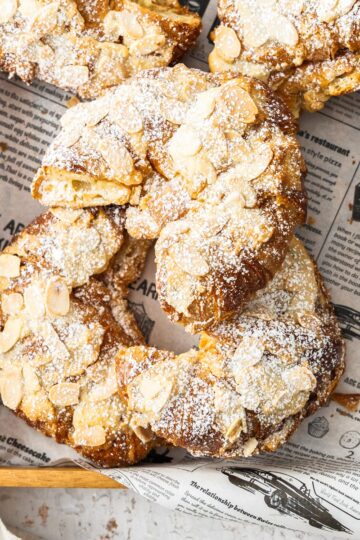 Top down view of five almond croissants on a wooden tray.