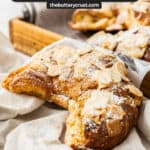 Closeup of an almond croissant in front of a wooden serving tray.